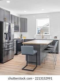 CHICAGO, IL, USA - SEPTEMBER 1, 2022: A Kitchen With Dark Grey Cabinets, Large Island With A Wood Countertop, And Stainless Steel Appliances.