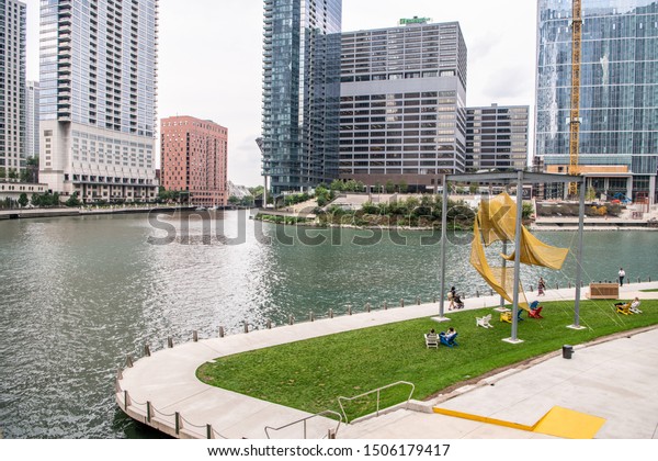 Chicago, IL / USA - September 11, 2019: People\
enjoy the day at a grassy area along Riverwalk, downtown, near the\
new public art installation, Black Tibernius by  Robert\
Burnier.