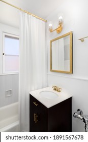 CHICAGO, IL, USA - SEPTEMBER 7, 2019: A White Bathroom With Dark Vanity And A Gold Light Fixture, Faucet, And Mirror.