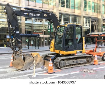 CHICAGO, ILLINOIS - MARCH 11, 2018: John Deere 75G Midsize Excavator With Dozer Blade Staged Next To Solar Powered Traffic Signature S Dearborn St Fiber Optic Excavation Trench And Bicycle Lane.