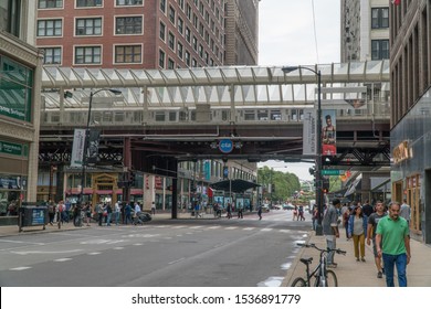 Chicago, Illinois, USA - Circa 2019: View Of Downtown Street Corner Intersection During Morning Rush Hour Commute Loop Train Passing On Overhead Track Past Buildings