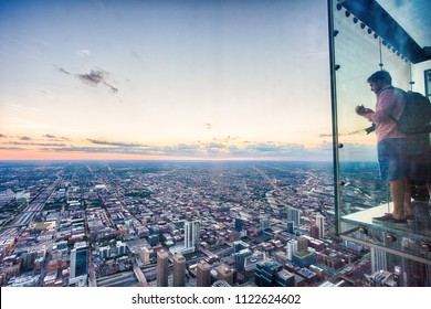 Chicago, Illinois, USA - June 2016: A tourist takes a picture of the Chicago skyline from one of the glass boxes of the Willis Tower Skydeck Ledge near sunset