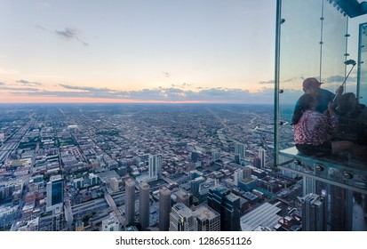 Chicago, Illinois, USA - June 2016: Tourists Taking Selfies From One Of The Glass Boxes Of The Willis Tower Skydeck Ledge. The Chicago Skyline Is Visible Near Sunset