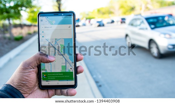 Chicago, IL/United States-May 10 2019:  Uber\
customer using the Uber app to help find a ride reach his\
destination in the big city of Chicago.  he stands outside as cars\
pass by and waits for his\
ride