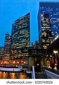 Chicago, IL/USA - 2/7/2018: City Night Lights Illuminate On A Nearly Frozen Chicago River As Elevated Train Passes Over Snow Covered Lake Street. Stairs Lead To River Bridgehouse.