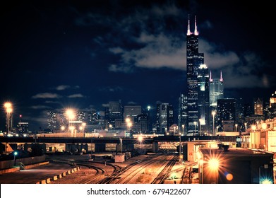 Chicago Skyline Cityscape At Night Featuring A Train Yard And Urban Bridge With A Dramatic Cloudy Sky.