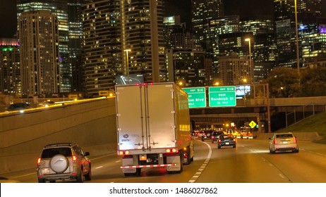 CHICAGO, UNITED STATES - 20 OCTOBER 2016: POV Driving Under The Overpass Bridge Along The Busy Jammed Multiple Lane Interstate Highway Towards Iconic Downtown Chicago City Skyscrapers Lit At Night