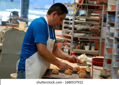 Chicago,IL/USA-July 1st 2019: Hispanic Male Blue Collar Bakery Chef Worker Is In The Process Of Kneeing Dough And Various Ingredients For His Pastry Shop. Local Homemade Desserts Are Cooked Perfectly