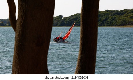 Chichester Harbour, England, UK. August 18th, 2022. Sailing Boat Seen Tilting On The Choppy Water, Framed By Two Tree Stems.