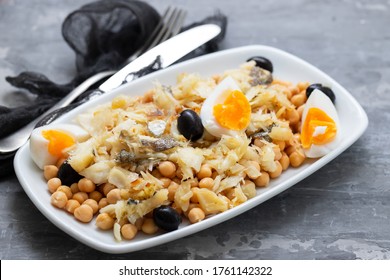 chick peas with cod fish, olives and boiled egg in white dish on ceramic background