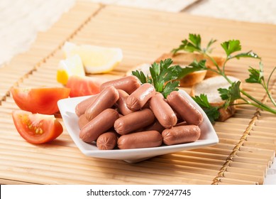 Chicken & Beef Cocktail Sausage With Cherry Tomato Radish And Lemon With Green Herb With Toast Bread On Green Red And Bamboo Background  With White And Green Plate