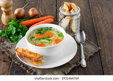 Chicken bouillon in the white bowl on the rustic wooden background served with croutons