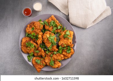 Chicken breaded breasts, fried in deep oil, golden color rich with flavors, served with ketchup and mayonnaise sauce, on a grey plate and grey background.