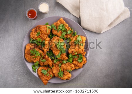 Chicken breaded breasts, fried in deep oil, golden color rich with flavors, served with ketchup and mayonnaise sauce, on a grey plate and grey background.