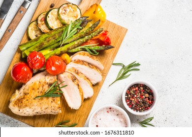 Chicken breast grilled with vegetables on a wooden serving board. Barbecue dish. Top view on white stone table. - Powered by Shutterstock