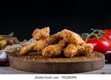 Chicken breast nuggets with vegetables on wooden background. Pile of crispy homemade baked chicken nuggets cooling.