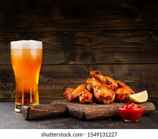 Chicken buffalo wings, beer in glass, lemon and ketchup sauce on wood board on wood dark background