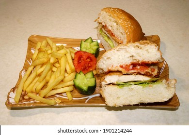 A Chicken Burger Split In Halves, Served With Crunchy French Fries, Cucumber And Fresh Tomato Salad