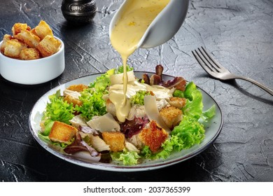 Chicken Caesar salad with the classic dressing being poured, croutons, and pepper, on a black background