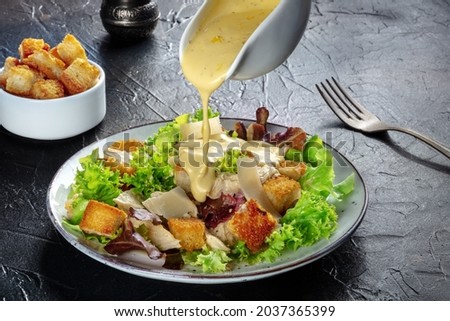 Chicken Caesar salad with the classic dressing being poured, croutons, and pepper, on a black background