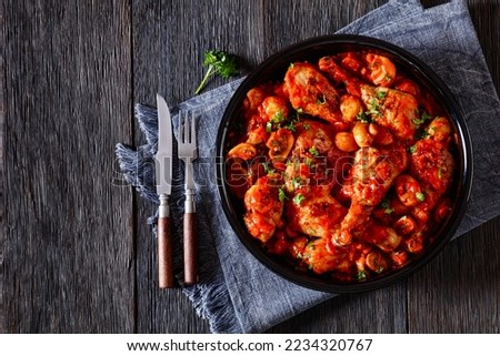 Chicken Chasseur, hunter chicken, poulet saute chasseur, chicken stew with mushrooms in tomato sauce in black bowl on wooden table, french cuisine, horizontal view from above, flat lay, free space