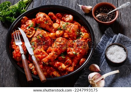 Chicken Chasseur, hunter chicken, poulet saute chasseur, chicken stew with mushrooms in tomato sauce in black bowl on wooden table, french cuisine