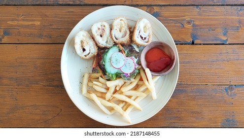 Chicken Cordon Bleu Served With Petit Peas And Baby Corn Salad With Herb Fries And Chili Dipping Sauce, On A Wooden Rustic Table 