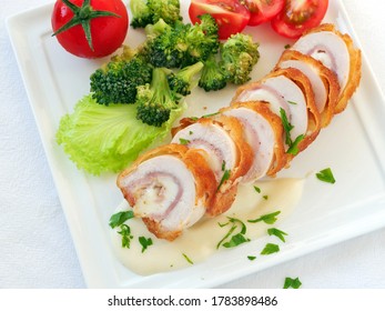 Chicken cordon bleu sliced with creamy white sauce and vegetables, top view, flat lay