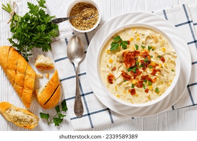 Chicken Corn Chowder, rich and creamy soup with leftover chicken breast, potatoes, sweet corn, topped with fried crispy bacon and fresh parsley in white bowl on wooden table, flat lay