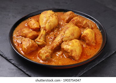 Chicken curry or masala,Kerala style chicken curry using fried coconut in traditional way and arranged in a black  ceramic vessel which is placed on a graphite sheet with grey background,isolated.