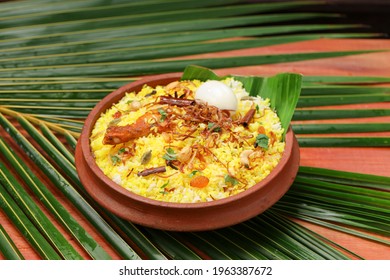 Chicken Dum Biryani , Arranged In An Earthen Ware And Placed On Coconut Leaf With Wooden Background.