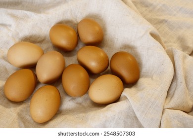 Chicken eggs on fabric tablecloth in rustic kitchen. Close-up brown eggs with crumpled fabric for daily and organic food, protein, cozy, cooking, and eating healthy concept. A group of eggs warm light - Powered by Shutterstock