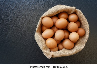 Chicken eggs in sack bag on rustic black background.