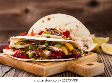 Chicken fajitas with grilled onions and bell peppers and serve with flour tortillas on rural wooden board