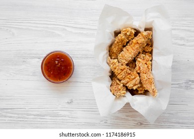 Chicken Fingers In Paper Box With Sweet Chili Sauce On A White Wooden Surface, Top View. Flat Lay, From Above, Overhead. 