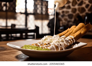 Flautas de pollo con queso y crema acompañados de guacamole en un restaurante típico mexicano de comida