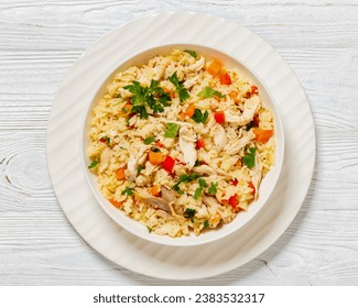 Chicken Fried Rice with red pepper, carrots and onion in white bowl with spoon and fork on white wooden table, horizontal view from above, flat lay, close-up