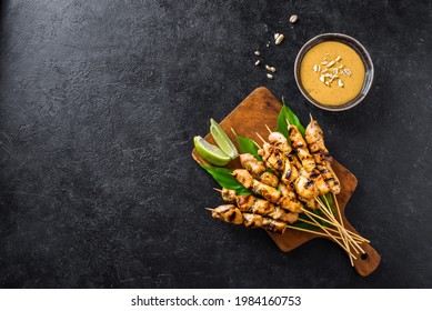 Chicken grilled satay skewers served with lime and peanut sauce on black, copy space. Asian thai style food.