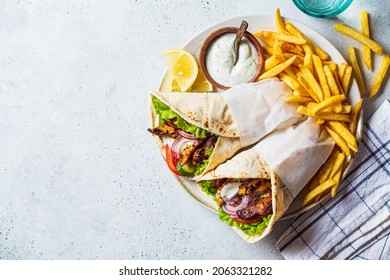 Chicken gyros with vegetables, french fries and tzatziki sauce on a plate, top view. Greek food concept.