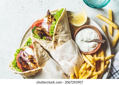 Chicken gyros with vegetables, french fries and tzatziki sauce on a plate, top view. Greek food concept.