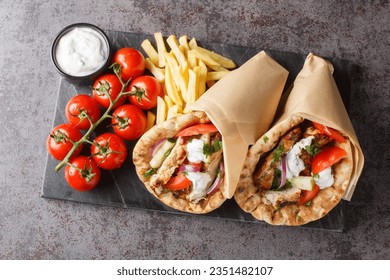 Chicken gyros with vegetables, french fries and tzatziki sauce closeup on the board on the table. Horizontal top view from above
