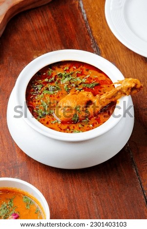 Chicken handi curry leg piece on top garnish with chopped coriander on restaurant wooden table indian food menu side view photography