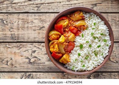 Chicken jalfrezi Indian spicy curry chilli meat with basmati rice and vegetables healthy dietetic asian food in clay dish on vintage table background.
