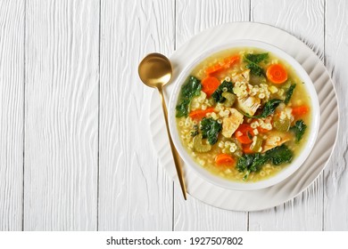 chicken kale soup with pasta anellini and vegetables in a white bowl with golden spoon on a wooden table, flat lay, free space, italian cuisine - Shutterstock ID 1927507802