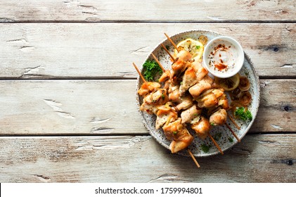 Chicken kebabs on skewers and savory cream sauce on grunge plate on natural wooden table. Flat lay. Copy space. Food for a picnic