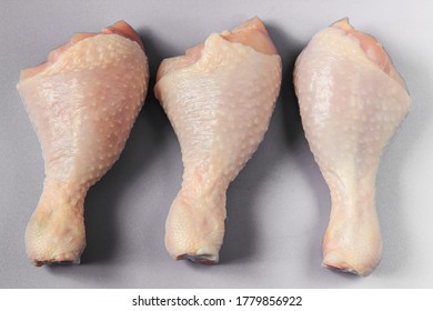 Chicken legs, arranged in a row of three raw chicken drumsticks on a light gray background, chicken raw meat, top view. 