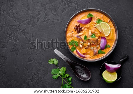 A Chicken Massaman Curry in black bowl at dark slate background. Massaman Curry is Thai Cuisine dish with chicken meat, potato, onion and many spices. Thai Food. Copy space. Top view