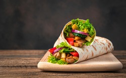 Chicken Meat, French Fries, Vegetables And Salad Are Wrapped In Pita Bread On A Brown Background. Traditional Shawarma. Side View, Copy Space.