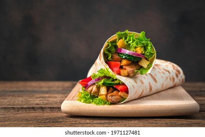 Chicken meat, French fries, vegetables and salad are wrapped in pita bread on a brown background. Traditional shawarma. Side view, copy space. - Powered by Shutterstock