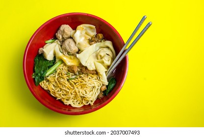 Chicken noodle or mie ayam in Indonesian, on red bowl with metal chopsticks with yellow background
